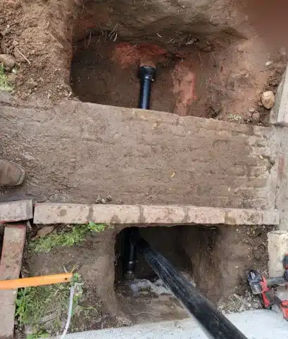 Excavated trench showing black sewer pipe through brick
